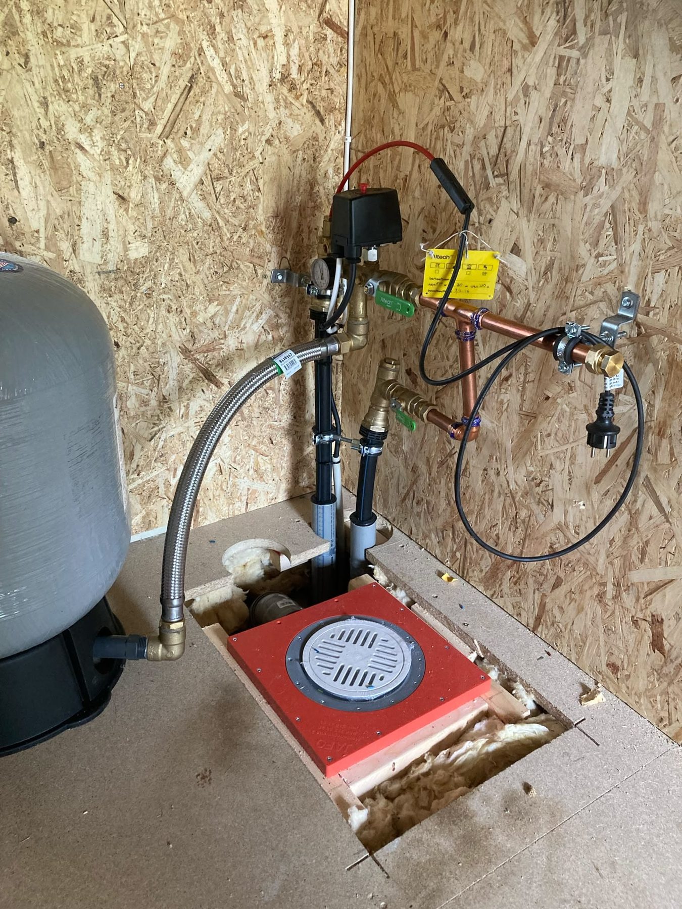 De waterpomp en het filter tegen een houten wand, met de put open in de vloer