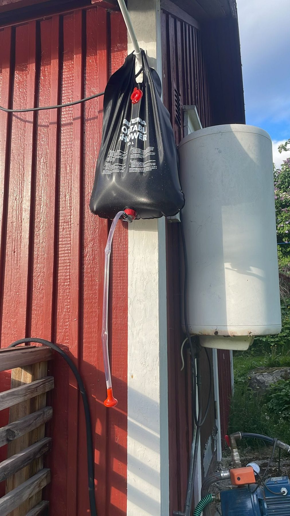 Een zwarte zonnedouchezak en een watertank aan de rode buitenmuur van het huis
