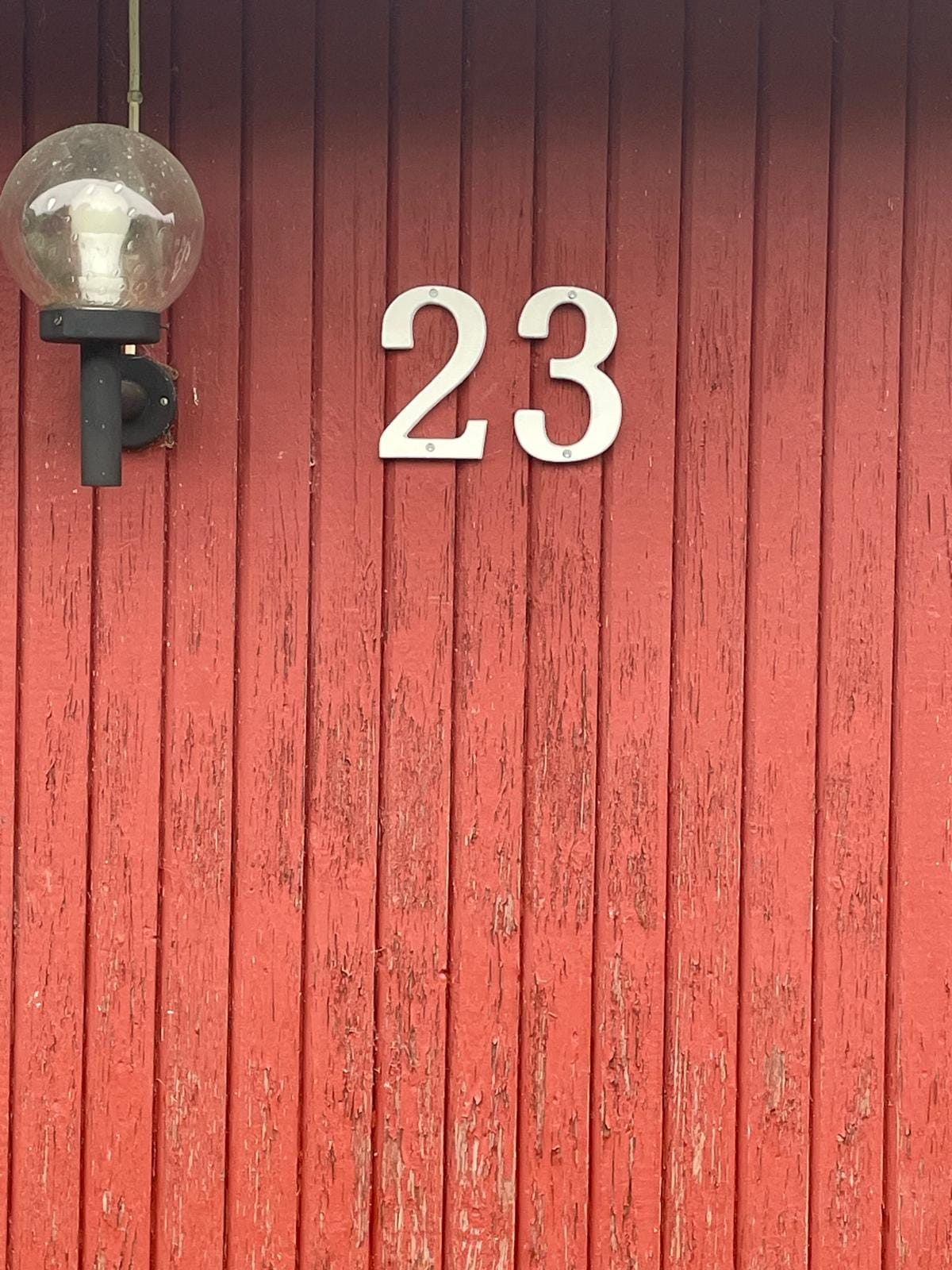 Huisnummer 23 in witte cijfers op de rode houten gevel, met een buitenlamp ernaast